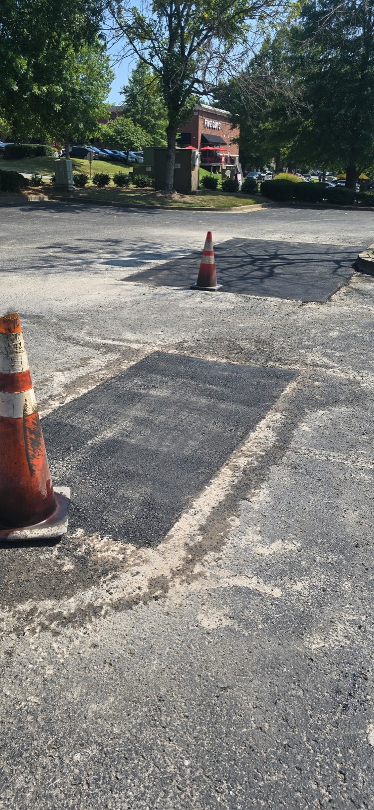 Two completed full-depth asphalt patches in a commercial parking lot, coned off while they set