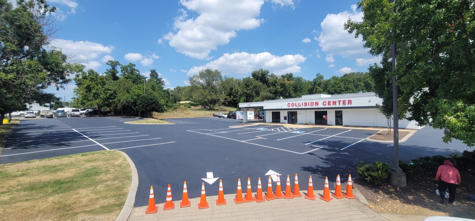 A commercial parking lot immediately after sealcoating and restriping, with fresh black surface, crisp white stall lines and directional arrows, coned off while it sets
